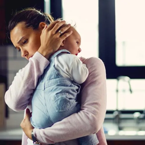Young worried mother comforting her crying baby at home.
